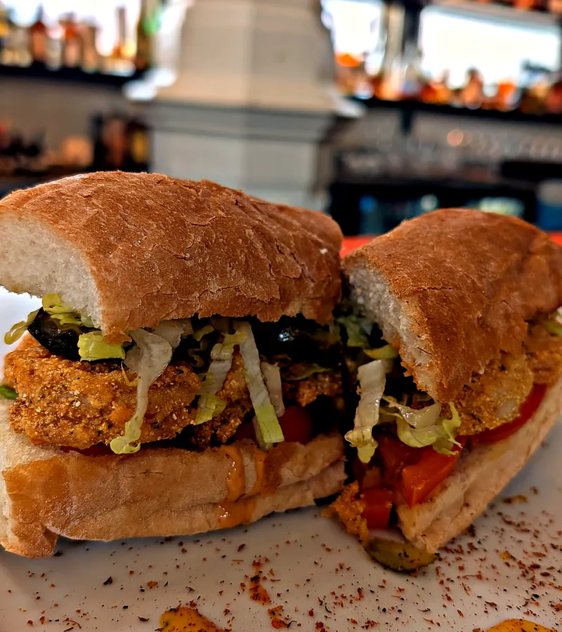 The fried oyster po-boy in two halves on a plate at the oyster bar, with one of the market's white cast iron columns and the back bar behind it