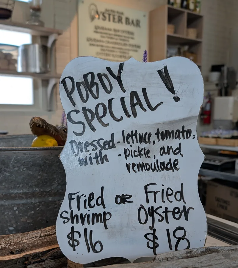 A hand-lettered white chalkboard sign at Salted Pearl reading Poboy Special, dressed with lettuce, tomato, pickle, and remoulade, fried shrimp sixteen dollars or fried oyster eighteen dollars